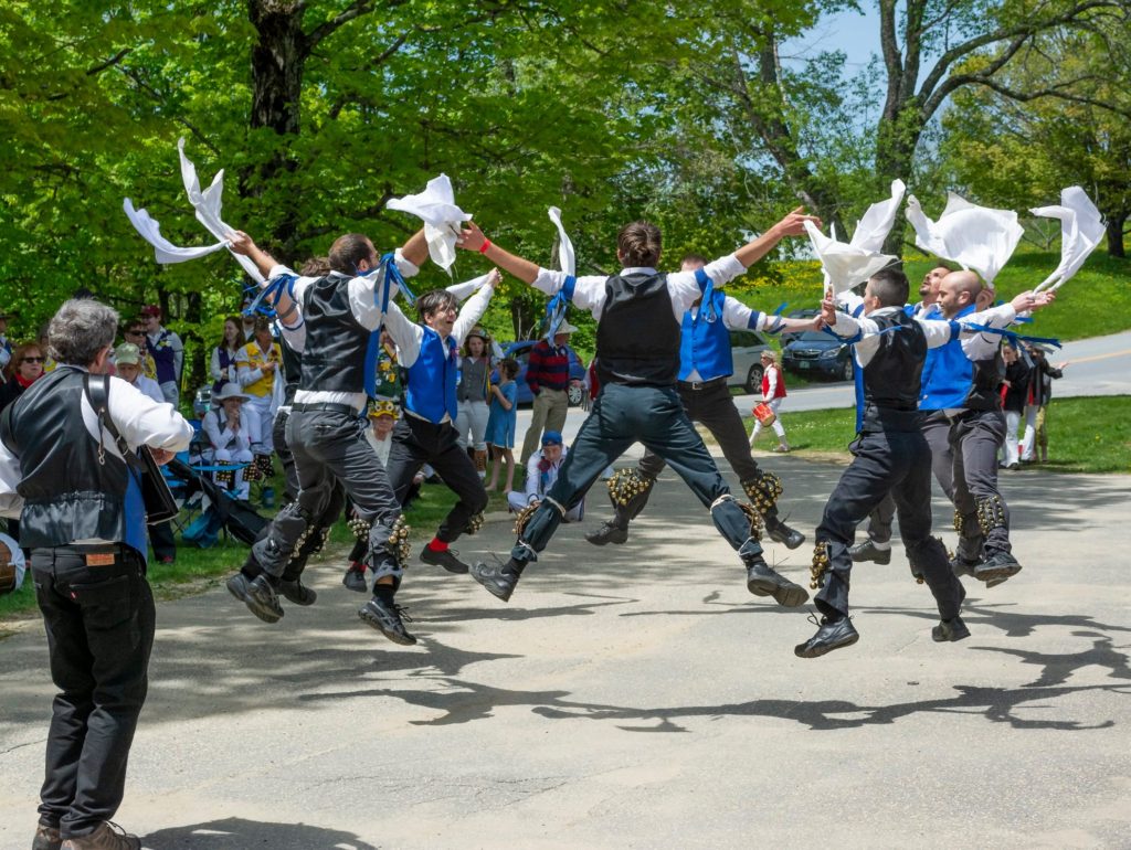 A photograph of Windham dancing in the Lichfield morris tradition in the sunlight with leafy trees behind them.